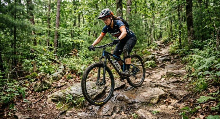 Rider on a lightweight aluminum hardtail mountain bike navigating a rocky forest trail