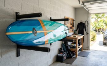 A surfboard mounted horizontally on a padded wall rack inside a clean, shaded garage
