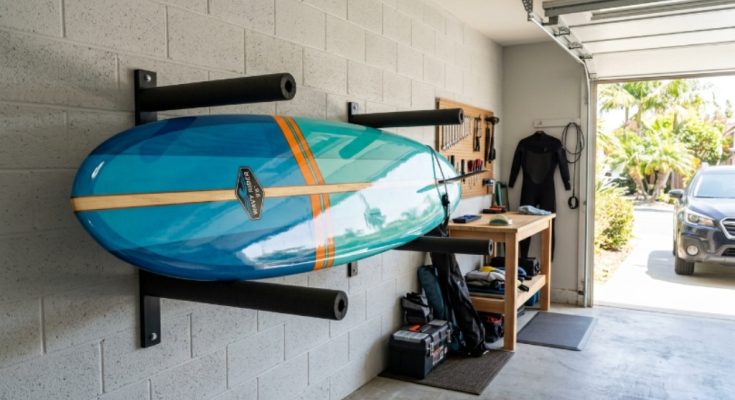 A surfboard mounted horizontally on a padded wall rack inside a clean, shaded garage